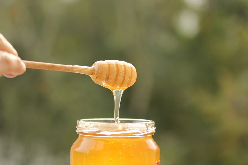 honey dripping from wooden dipper into jar