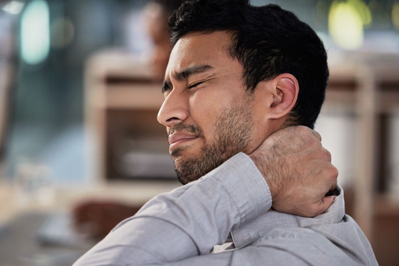 man experiencing neck pain rubbing his neck