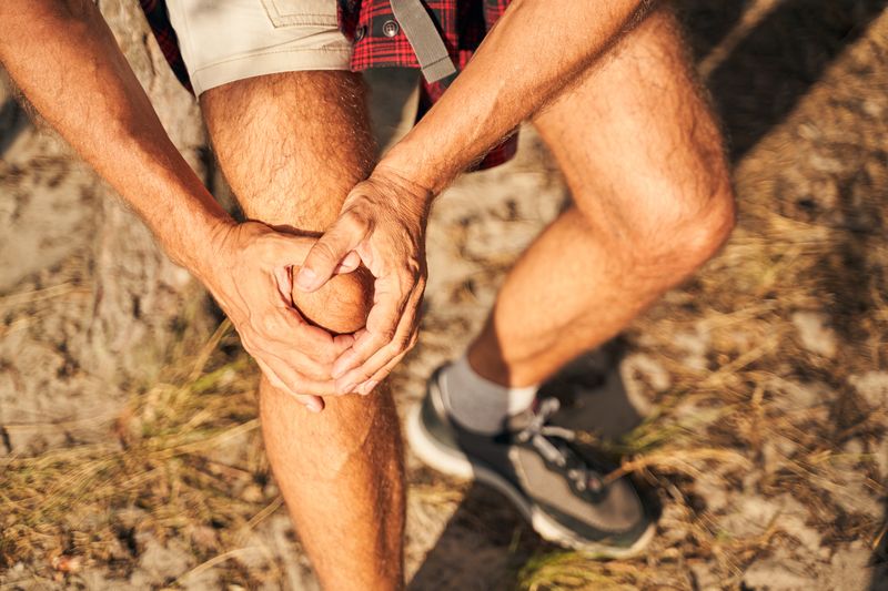 man holding knee in pain outdoors during day