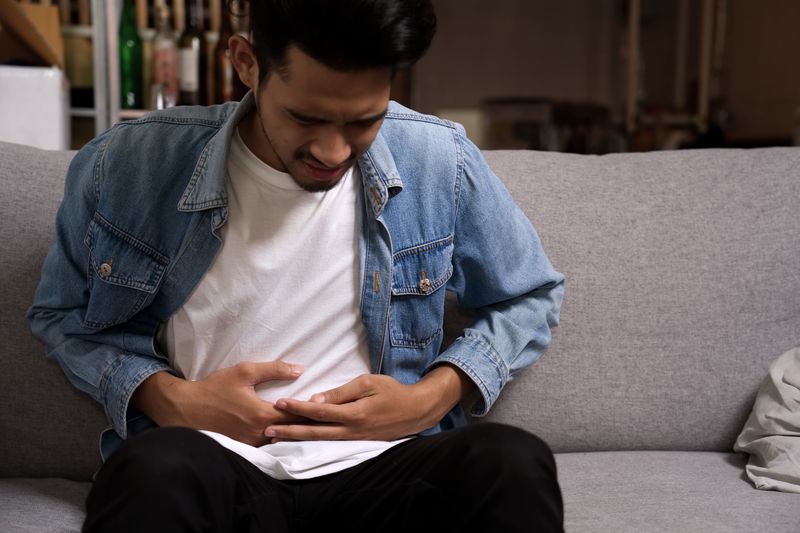 man on couch with stomach discomfort and pain