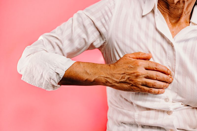 senior woman s hand over chest against pink backdr