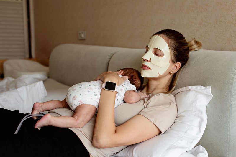woman relaxing with facial mask holding baby