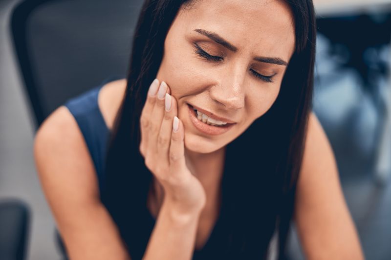 young woman suffering from toothache holding her